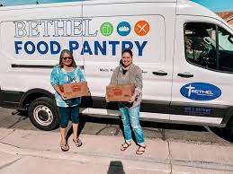 Two volunteers holding food boxes in front of the Bethel Community Church food pantry van