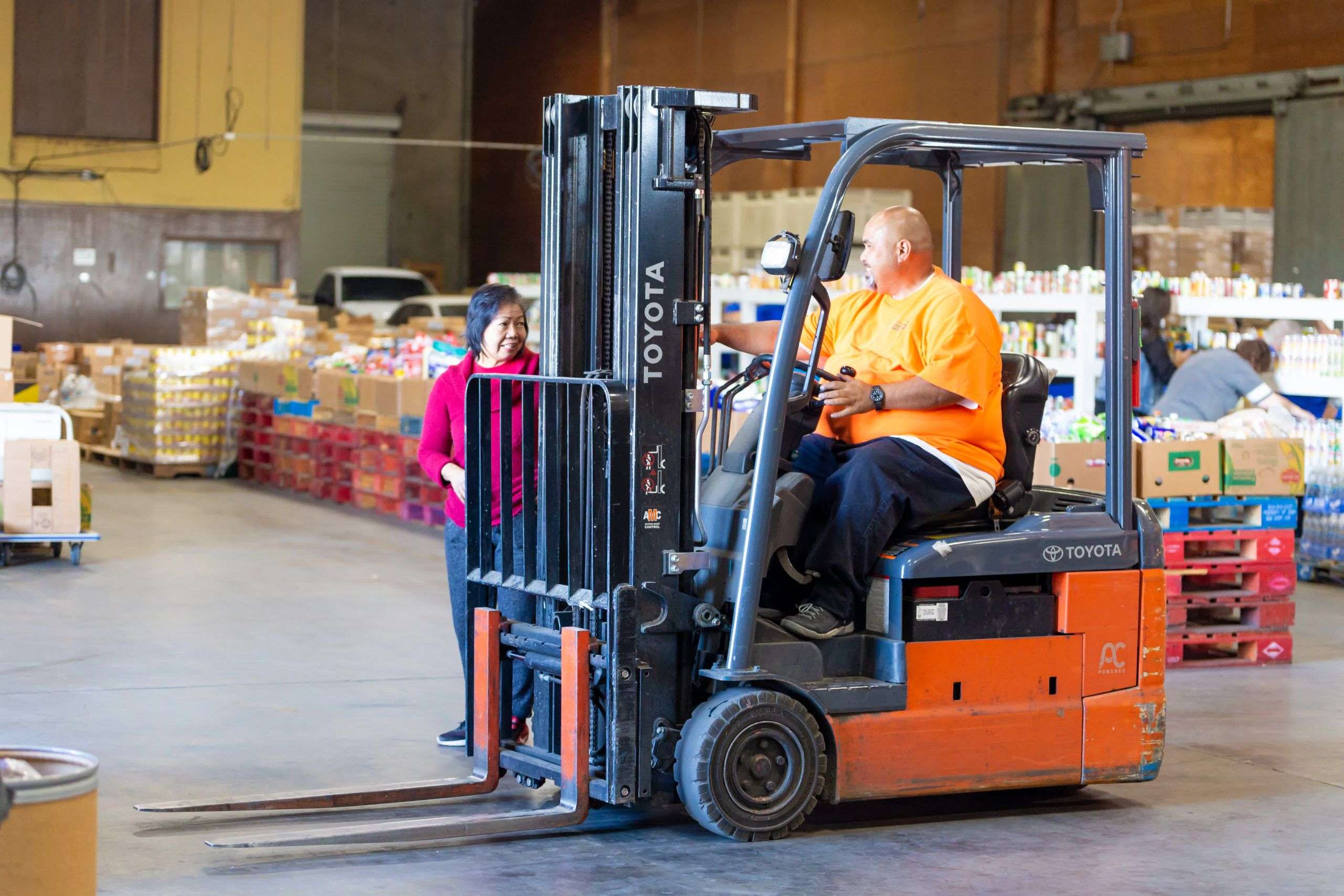 Worker in forklift stopped and talking with volunteer in the Merced County Food Bank warehouse