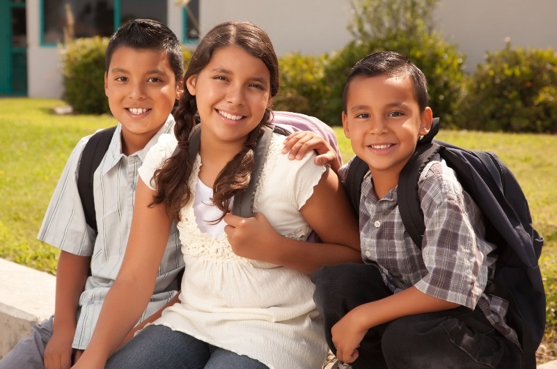 Two boys and a girl with backpacks witting on a bench