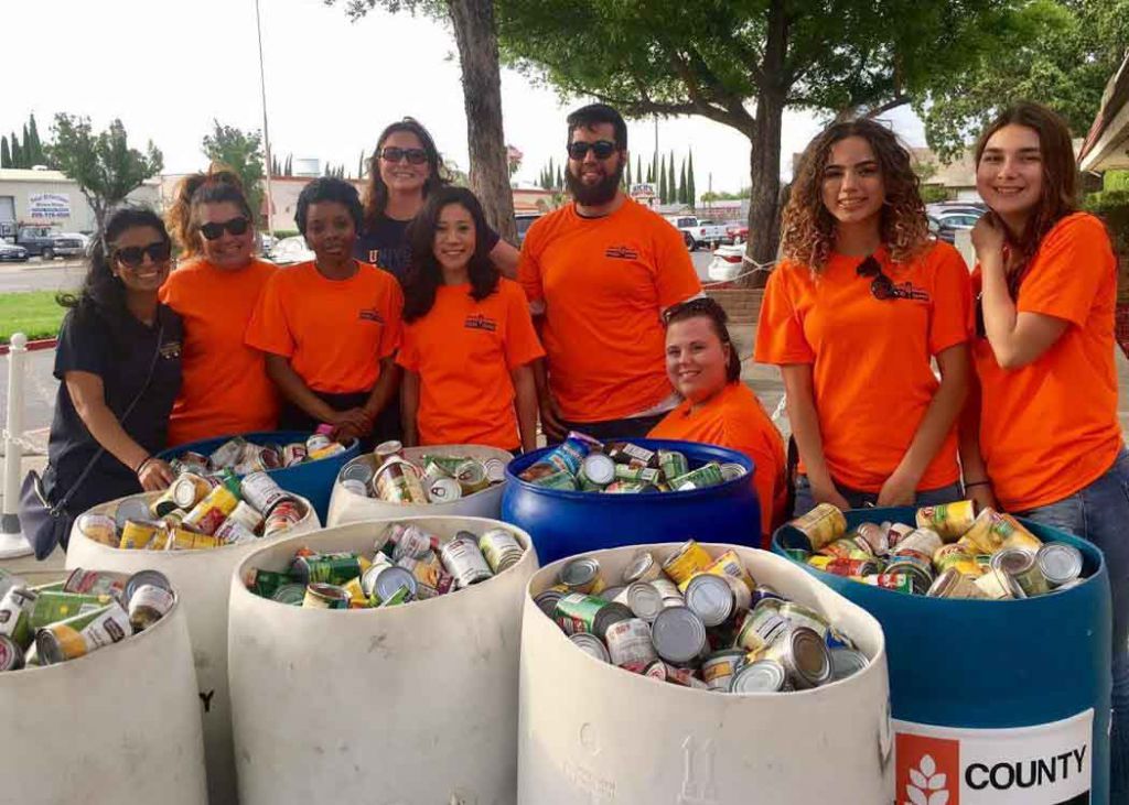 Volunteers for the Merced County Fair Annual Food Drive in front of containers filled with canned goods