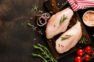 Fresh raw chicken meat fillet with salt, pepper, onion and butter on a wooden board on a dark wooden rustic background